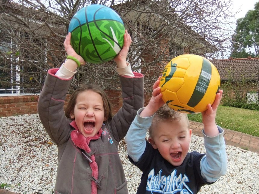 Dwójka dzieci radośnie krzyczy unosząc piłki nad głowami.