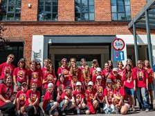 Na zdjęciu grupa młodzieży a w tle budynek Fabryki Aktywności Miejskiej. Po prawej stronie w niebieskiej koszulce Opiekun grupy.